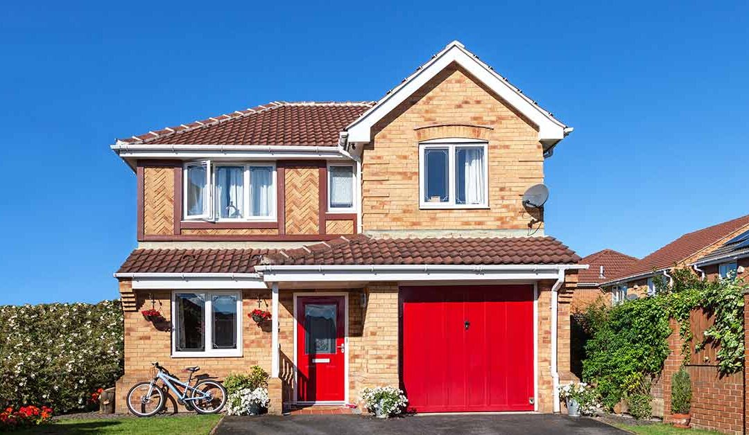 Ein Einfamilienhaus mit Backsteinwand und roter Garagentür vor blauem Himmel - Immobilie finden